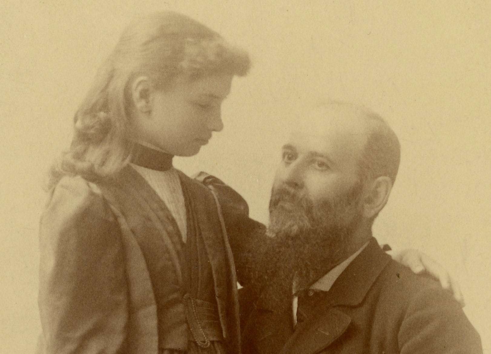 Michael Anagnos, seated with Helen Keller standing at his left with her arm around his shoulder and his arm around her waist. Michael Anagnos was the director at Perkins during the time Helen Keller was a student there and was responsible for sending Anne Sullivan to Alabama to work with her as a child