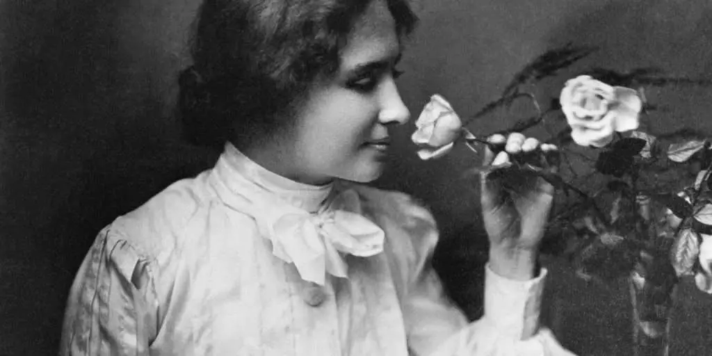 American writer and lecturer Helen Keller (1880 - 1968) takes time to smell a rose. Due to illness Keller suffered loss of sight and hearing at the age of 19 months. From a photograph by Whitman.